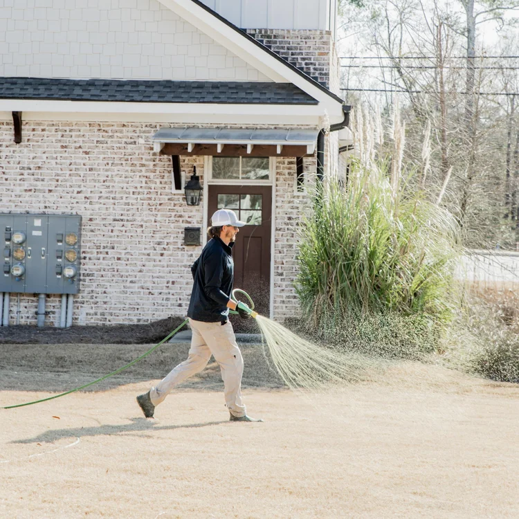 Matthews Turf Management technician treating a lawn in front of a residential home